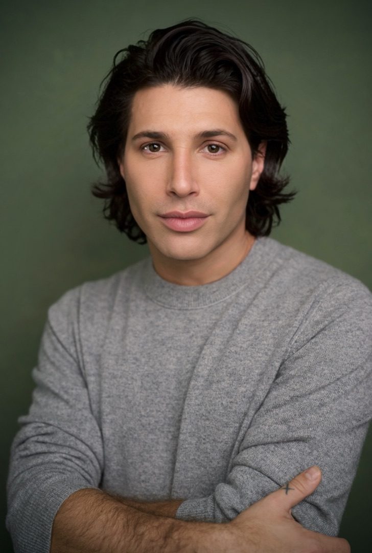 Noah Benjamin Miller in a gray sweater, arms crossed