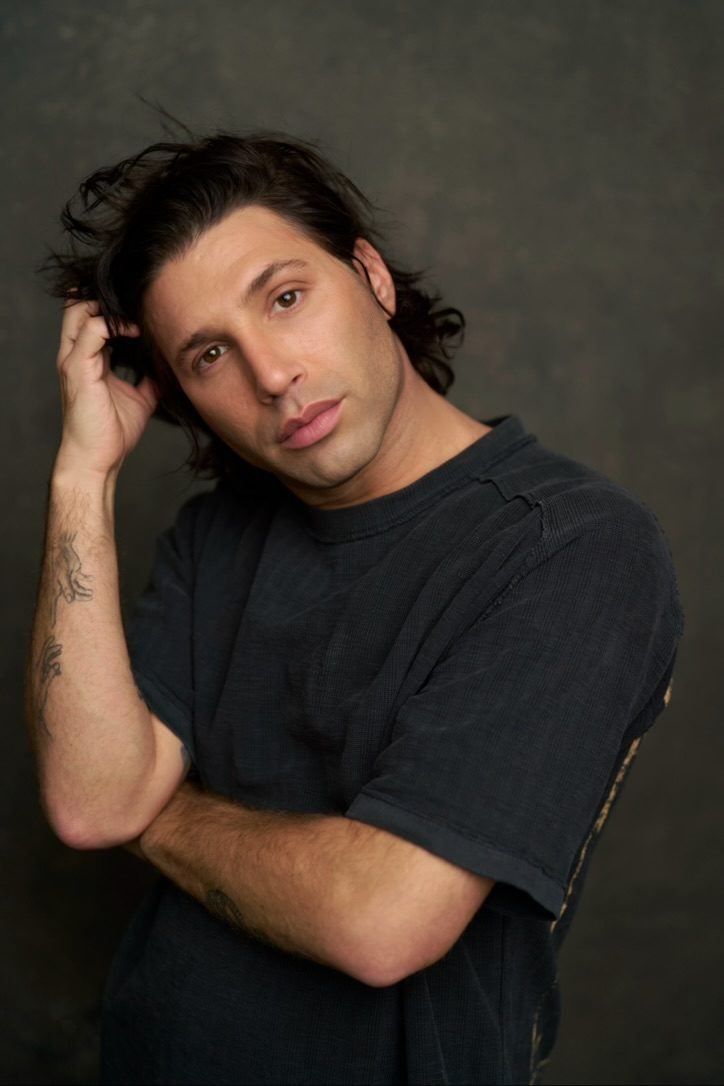 Noah with a hand in his hair, in a black tee